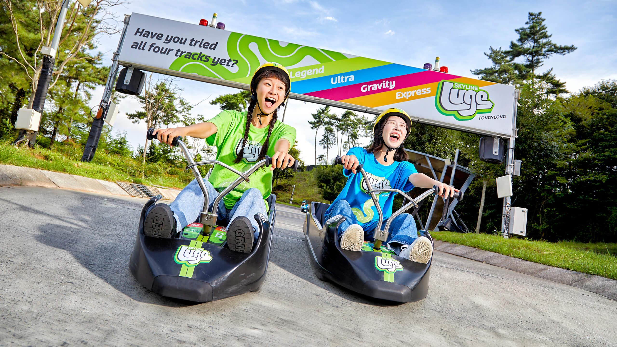 Two girls grin and scream as they ride down a steep section on the track at Skyline Luge Tongyeong.