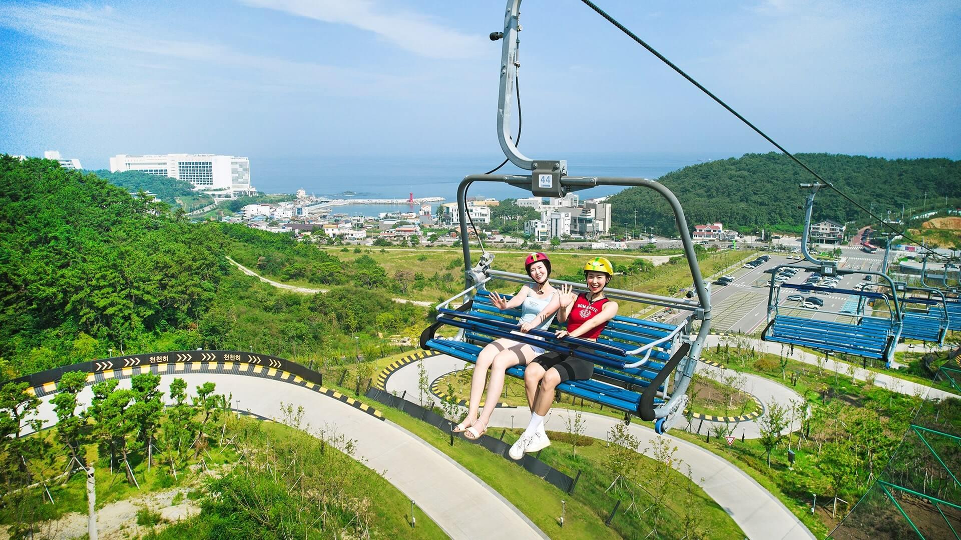 Two women ride the Skyline Luge Busan chairlift.