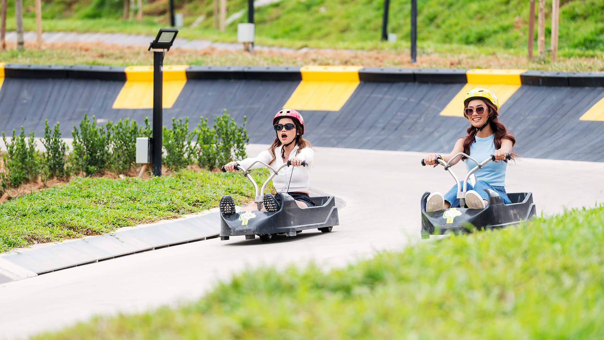 Two girls scream and smile as they descend the tracks at Skyline Luge Kuala Lumpur.