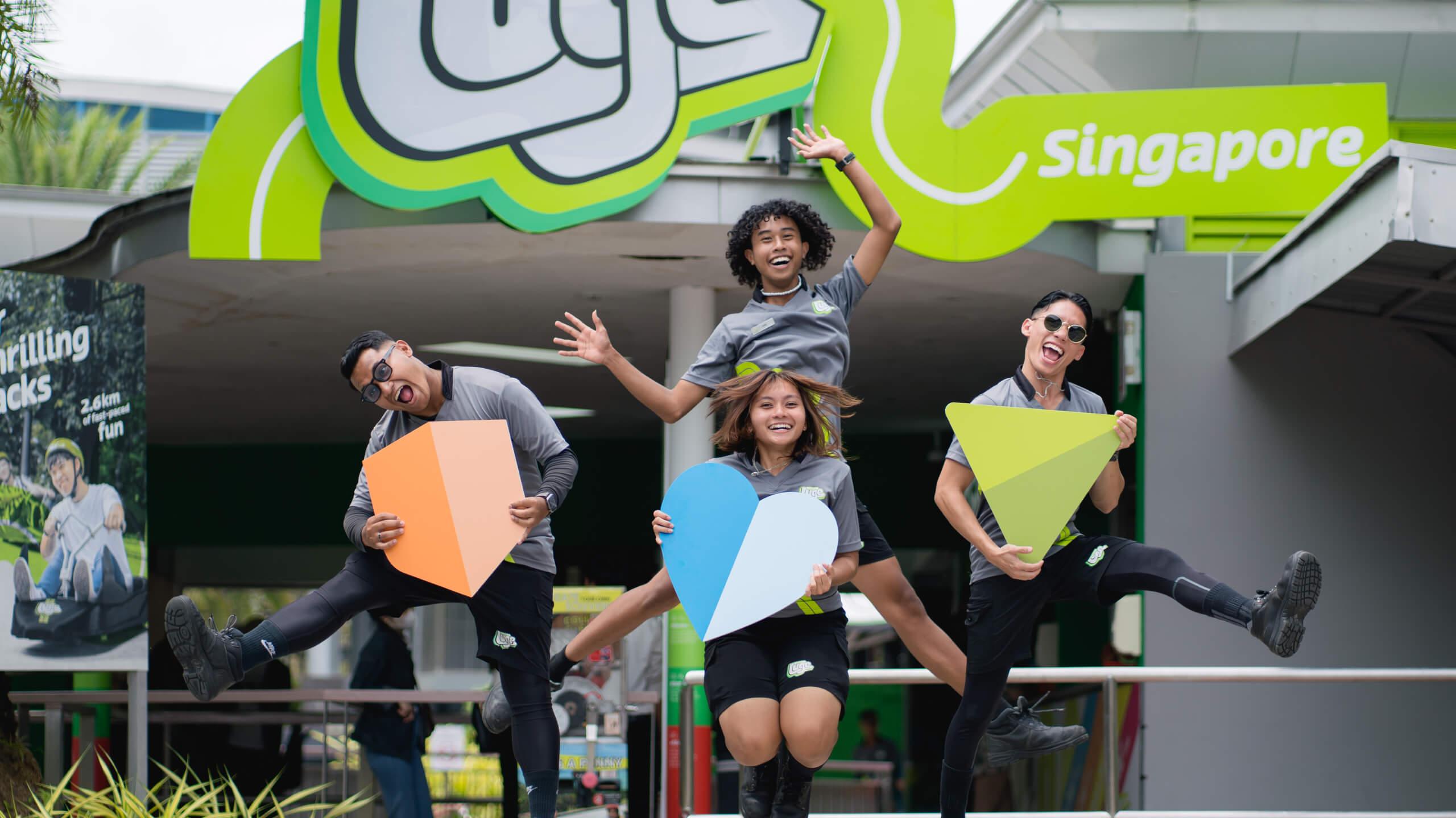 Four Skyline Luge Singapore employees jump in the air with colourful cardboard cutouts.