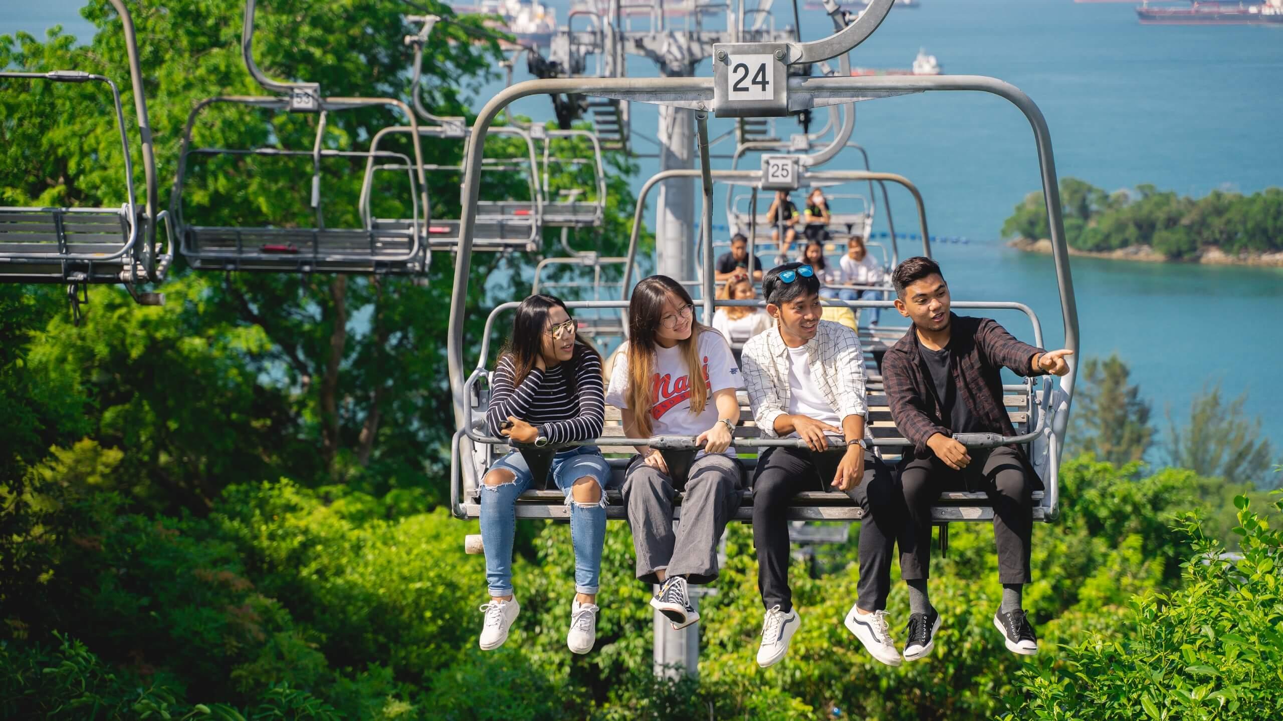 A group of friends point and look at something whilst riding the Skyride chairlift at Skyline Luge Singapore.