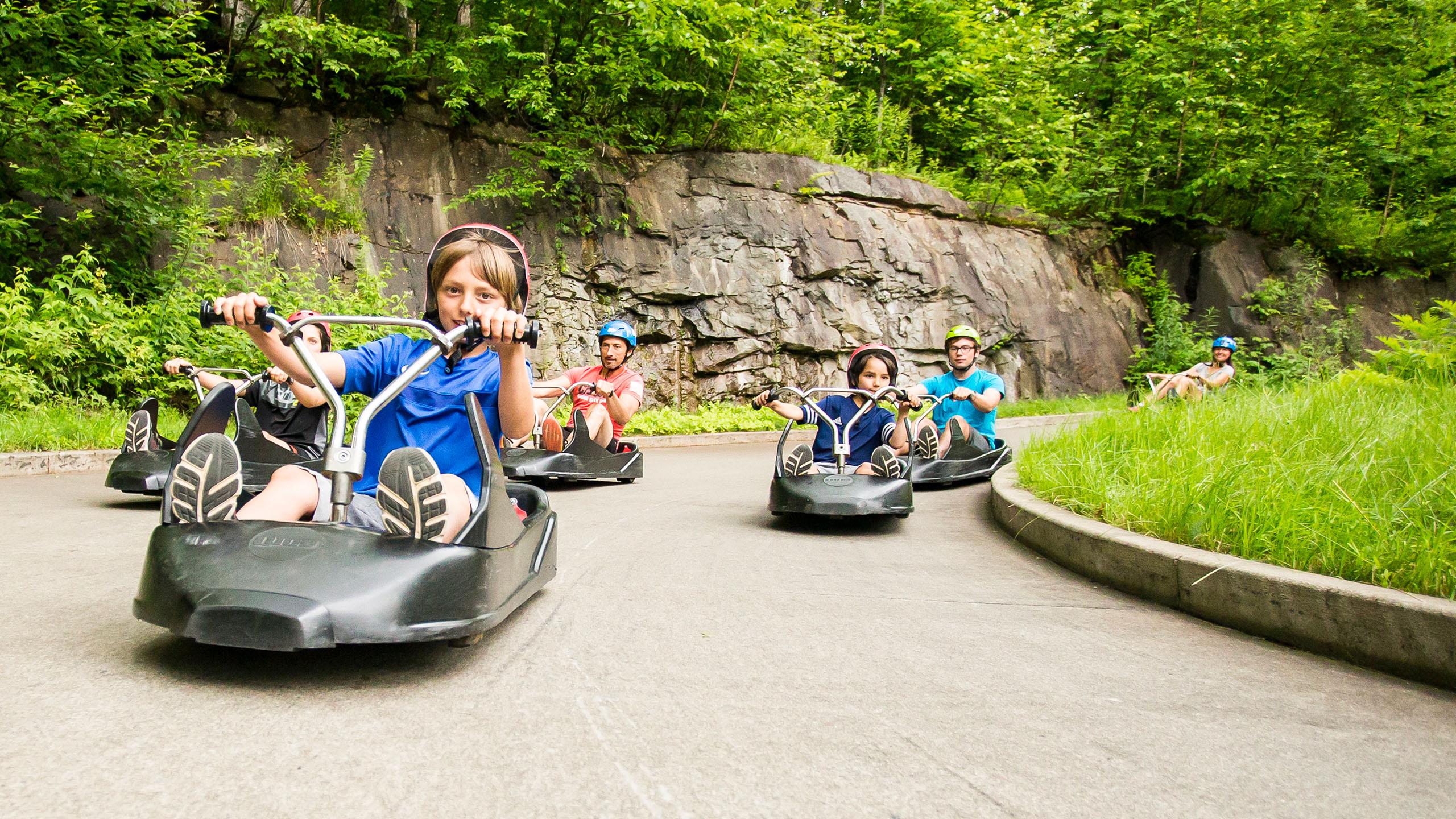A group of kids and adults race round a corner on the Skyline Luge Mont Tremblant track.