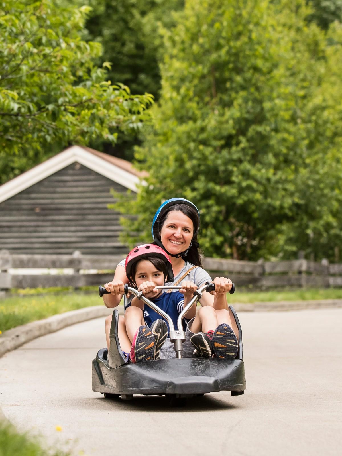 A mother and son smile as they cruise down the track together at Skyline Luge Mont Tremblant.