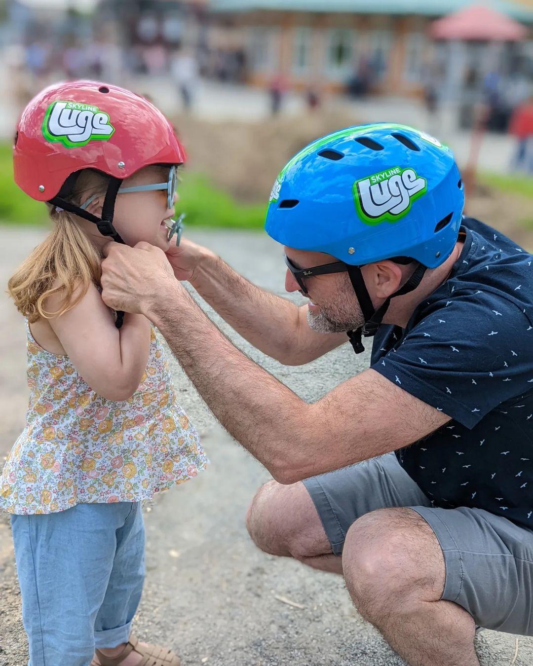 A father makes sure his daughters Luge helmet is tight and secure.